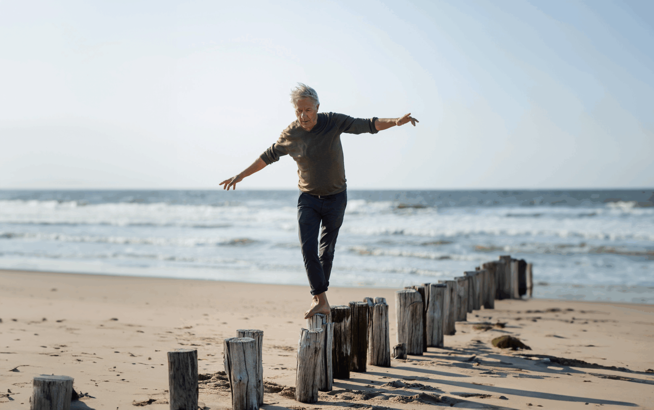Carefree senior man balancing on wooden posts at beach-Recovered